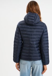 Chaqueta acolchada de color azul marino con capucha, que presenta secciones acolchadas horizontales. La tela tiene una textura suave y brillante.