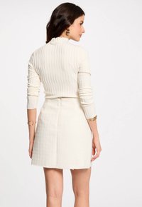Donna che indossa un top a coste crema con maniche lunghe e una gonna mini alta a vita, accessoriate con orecchini a cerchio dorati e bracciali.