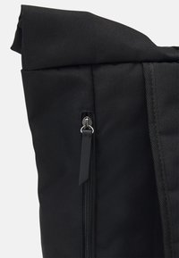 Black fabric backpack with a textured finish, roll-top opening, and a zippered pocket featuring a metal pull tab and accent stitching.