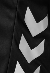 Czarna tkanina z trzema dużymi białymi kształtami szewronów skierowanych w dół, nadrukowanymi pionowo po prawej stronie.