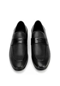 Zapatos negros sin cordones con textura de espiga, detalles de cuero suave, suelas planas y una correa estrecha en la parte superior para un ajuste seguro.
