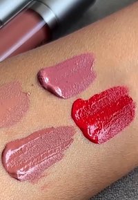 Fyra läppstiftsprover på armhud i nyanserna mauve, dammig rosa, nakenbrun och klar röd med ett läppstiftsrör vid överkanten.