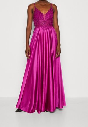 Femme portant une robe longue en satin rose vif avec un corsage en dentelle perlée et de fines bretelles.