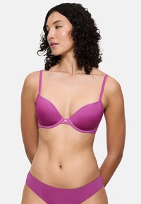 Lyserød formstøbt bh med justerbare stropper og en gylden detalje i midten. Stoffet fremstår glat og let skinnende, hvilket forbedrer dets samlede udseende.