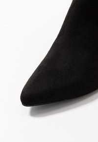 Acercamiento de la punta afilada de una bota de mujer de ante negro sobre un fondo blanco.