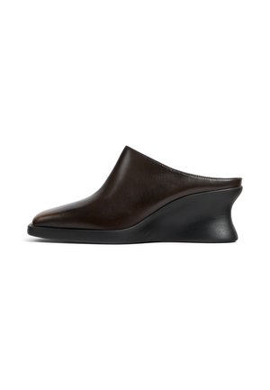 Mule in pelle marrone scuro slip-on con punta affilata e suola zeppa spessa curva nera su sfondo bianco.