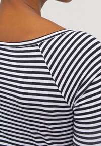 Närbild av en person som bär en svartvit randig skjorta, vilket visar baksidan av halsringningen och övre axelområdet.