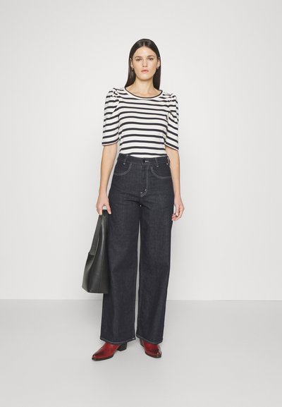 Striped black and white blouse with puff sleeves, paired with wide-leg dark denim jeans and red heeled boots. Holds a black tote bag.