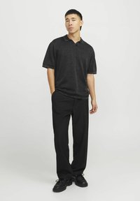 Polo noir à manches courtes avec col, associé à un pantalon noir fluide et des chaussures à lacets noires, sur un fond neutre.