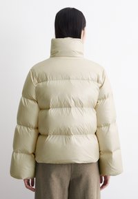 Kremfarget dunjakke med høy krage, quiltet design og overdimensjonerte ermer. Glatt, shiny materiale med en avslappet passform.