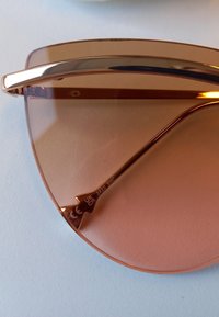 Růžové sluneční brýle s elegantním kovovým rámem. Skla jsou velká a zakřivená, s lesklým zlatým akcentem pod obočím.