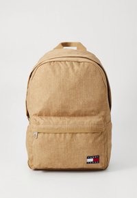 Khaki fabric backpack with a textured finish, a front zip pocket, and a logo patch at the bottom right. Features a padded top handle.