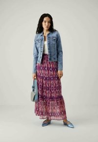 Heled denim jakk, valge topp, lilla mustriga maxi-seelik ja hele sinine tasapinnaline jalats. Hoides käes heledat halli käekotti. Sujuvad tekstuurid ja kihilise seeliku efekt.