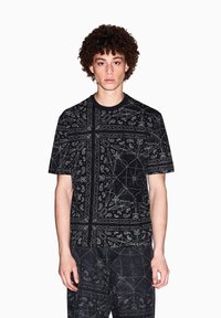 T-shirt di cotone nero con motivi paisley e geometrici bianchi, colletto tondo, maniche corte e vestibilità rilassata.