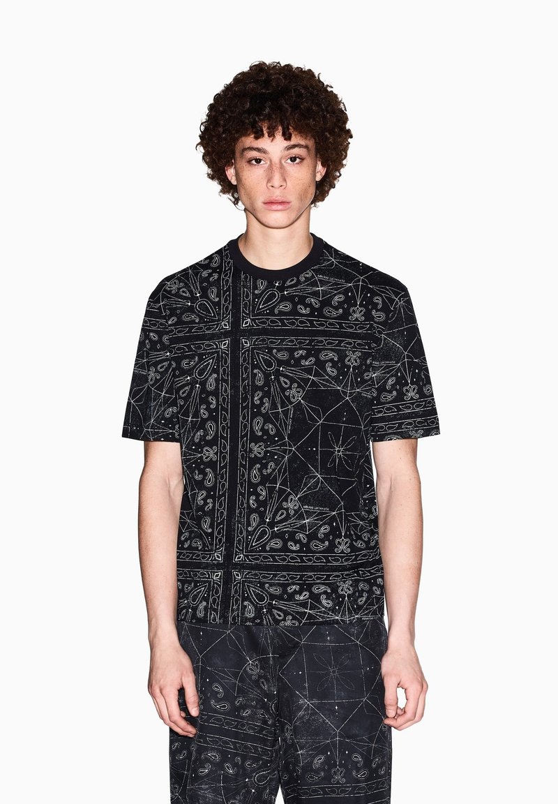 T-shirt di cotone nero con motivi paisley e geometrici bianchi, colletto tondo, maniche corte e vestibilità rilassata.