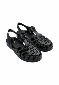 Czarne, błyszczące plastikowe sandały z plecionym wierzchem, regulowanym paskiem na kostce i płaską podeszwą. Posiadają pasek t dla dodatkowego wsparcia.