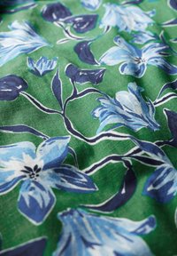 Tissu présentant de vibrantes fleurs bleues et de sombres feuilles sur un fond vert ; motif floral détaillé avec une texture lisse.