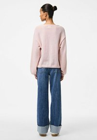 Ljusrosa oversized tröja, bakvy, parat med vida blå jeans med uppvikta fållar och subtil fransning i kanterna.