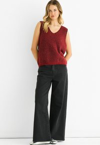 Red sleeveless knit sweater with a V-neck, textured with flecks, paired with high-waisted black wide-leg jeans and silver shoes.