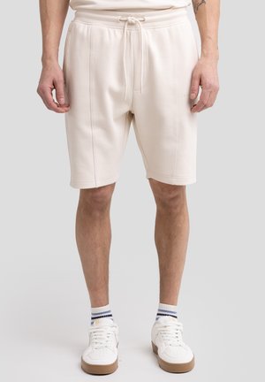 Lys beige bomuldsblandingsshorts med elastisk talje og snørebånd, sidelommer og dobbeltstikninger. Båret med hvide sneakers og stribede sokker.