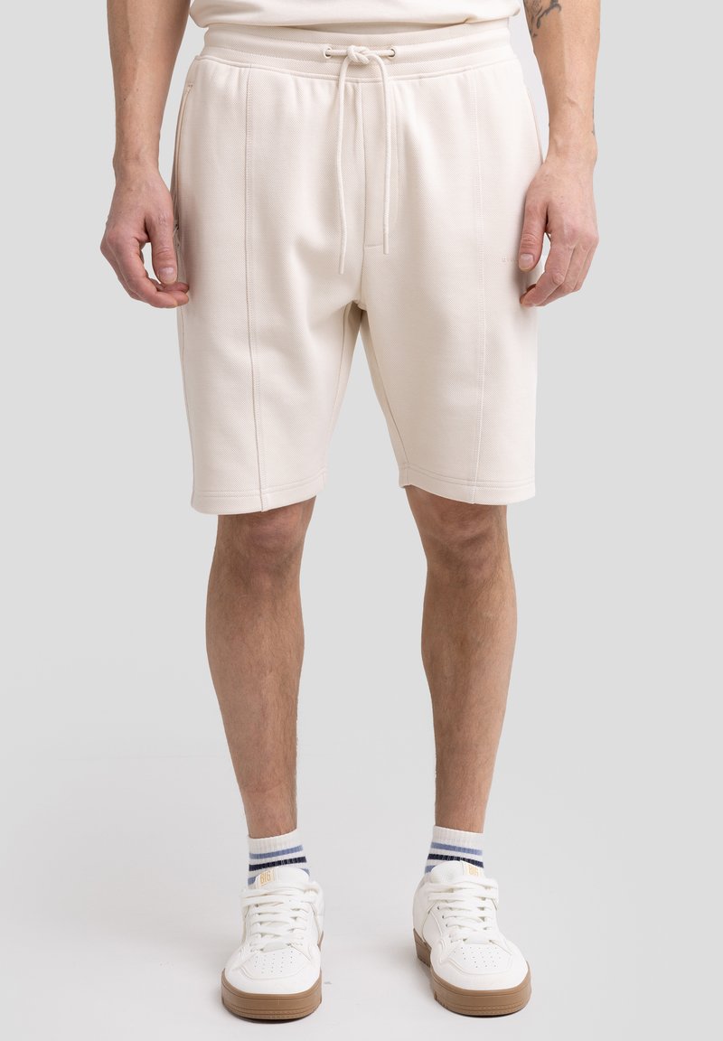 Lys beige bomuldsblandingsshorts med elastisk talje og snørebånd, sidelommer og dobbeltstikninger. Båret med hvide sneakers og stribede sokker.