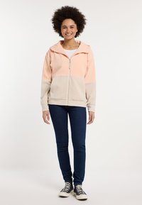 Contrast block hoodie in perzik en beige ribbelstructuur, met een volledige ritssluiting, trekkoord capuchon en lange mouwen. Gemaakt in combinatie met blauwe jeans.