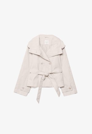 Oblečen svetlo bež krajšega dolgoročnega plašča s širokim ovratnikom, dvorednimi gumbi, pasom za zavezovanje v pasu in zapenjanimi manšetami na rokavih.