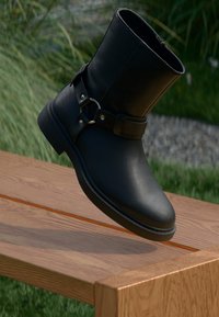 Must elastsest saapad ümarate varvastega, keskmise säärehaiusega, vöö ja pandla detailiga, sileda tekstuuriga ja tugeva madala kandaga.