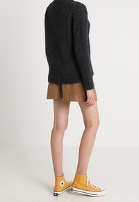 Dunkelgrauer, strukturierten Pullover mit Rundhalsausschnitt, kombiniert mit einem braunen Wildlederrock und gelben High-Top-Sneakern mit weißen Sohlen und Akzenten.