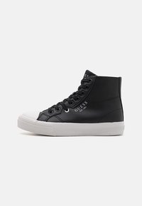 Mustad mustad spordijalatsid tekstureeritud naha pealmisega ja valge kummitald. Omab musti paelu ja külje peal "GUESS" brändi.