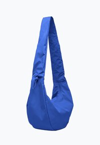 Bolso bandolera azul de nylon. Cuenta con una correa larga y ancha y un diseño de cuerpo curvado. Textura suave con cierre de cremallera y detalle anudado.