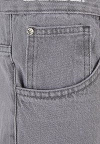 Gray denim fabric features a small front pocket with a silver metal rivet detail and stitched edges. The texture appears durable and structured.