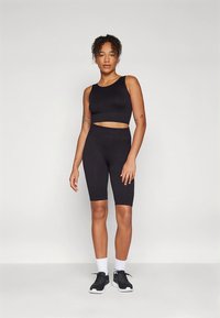 Fekete sportos két részes szett, mely crop topból és magas derekú biciklis rövidnadrágból áll, sima, rugalmas anyagból készült. A modell fekete sportcipőt és zoknit visel.