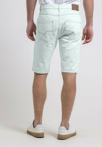 Shorts en denim vert menthe clair avec une coupe droite, poches arrière dotées d'un motif en V, et un patch en cuir marron sur la taille.
