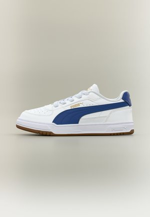 Balti žemo profilio Puma sportbačiai su tamsiai mėlyna juosta, baltais raišteliais ir ruda gumine sole, pateikti neutraliame fone.