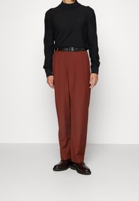 Schwarzer Rollkragenpullover, braune plissierte Hose mit einem Gürtel und glänzende schwarze Schuhe. Das Outfit hat eine lässige Passform und eine glatte Textur.