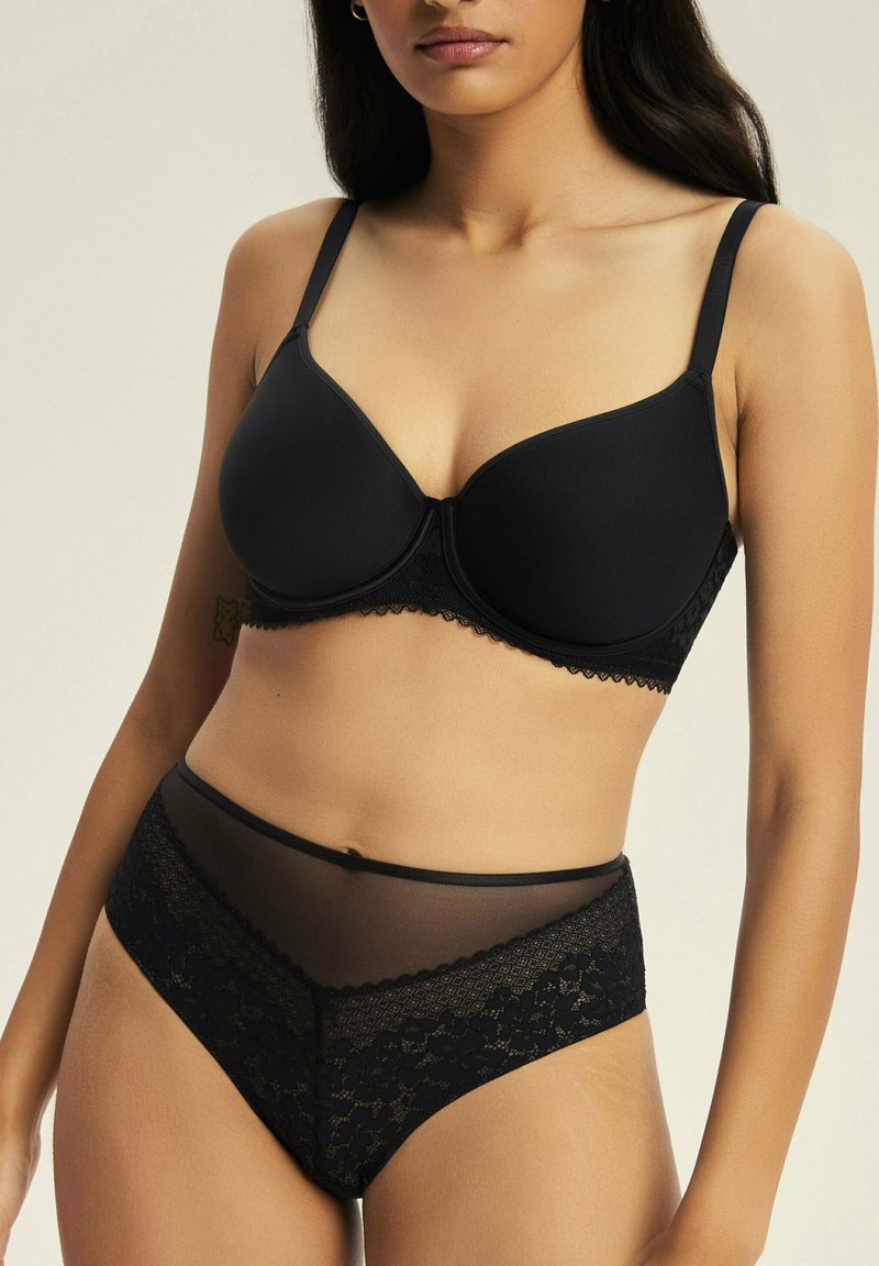 Czarny stanik z formowanymi miseczkami i koronkowym wykończeniem, zestawiony z czarnymi majtkami w wysokim stanie z przezroczystą siateczką i akcentami z koronkowych kwiatów.