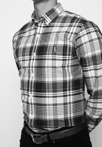 Svart och vit rutad skjorta i bomull med knapp-och krage, framknappar och en liten logotyp på bröstet. Buren med ett svart bälte.