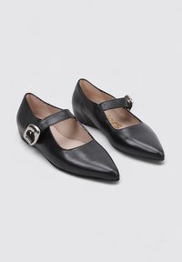 Zapatos Mary Jane de cuero negro con puntera puntiaguda, una tira ancha en el arco y un detalle de hebilla plateada. Tacón bajo en forma de cuña. Textura suave.