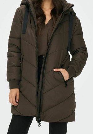Femme portant un manteau matelassé vert olive foncé avec capuche, fermeture éclair à l'avant, poches zippées et poignets côtelés.