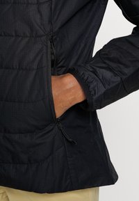 Černá vycpaná bunda s texturovaným povrchem, boční kapsa na zip a elastické manžety. Má elegantní, lehký design.