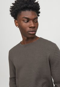 Camisa de manga larga texturizada de color gris oscuro con cuello redondo. Presenta un escote acanalado y un patrón sutil en toda la tela.