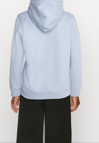 Jasnoniebieska bluza z kapturem o miękkiej fakturze, regulowany kaptur i ściągacze na rękawach, zestawiona z luźnymi czarnymi spodniami. Prosty design, bez wzorów.