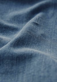 Denim-kangas syvässä sinisessä sävyssä, joka esittelee pehmeää rakennetta ja hienovaraisia vaihteluita kudonnassa ja pinnan sileydessä.