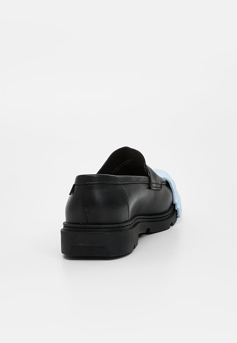 Scarpa nera in pelle slip-on con punta arrotondata, dotata di un accento in gomma blu testurizzata sul lato e una suola nera piatta.