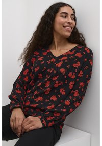Zwarte blouse met rood bloemenpatroon, V-hals, lange mouwen en geraffineerde manchetten. Gladde stof met een relaxte pasvorm.