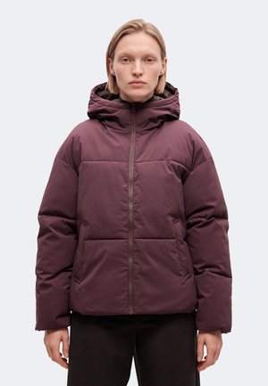 Un mannequin se tient devant un fond clair, vêtu d’une veste matelassée couleur prune avec une grande capuche, une fermeture éclair sur le devant et des poches latérales.