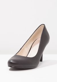 Chaussure à talon haut en cuir noir avec un bout arrondi, surface lisse et un talon fin. L'intérieur a un revêtement de couleur claire.