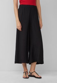 Zwarte wijde culottes gemaakt van lichtgewicht, gestructureerde stof met een elastische tailleband. Gecombineerd met platte zwarte sandalen.