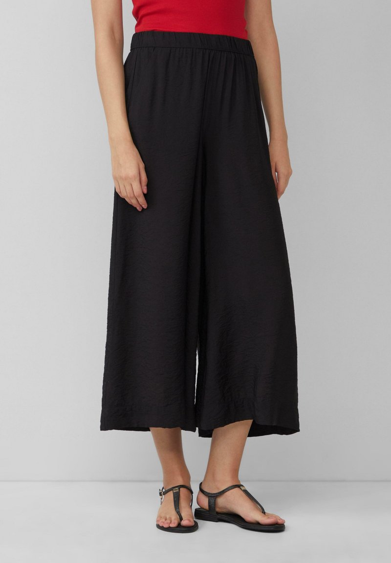 Culotte neri a gamba larga realizzati in un tessuto leggero e strutturato, con vita elastica. Abbinati a sandali neri piatti.